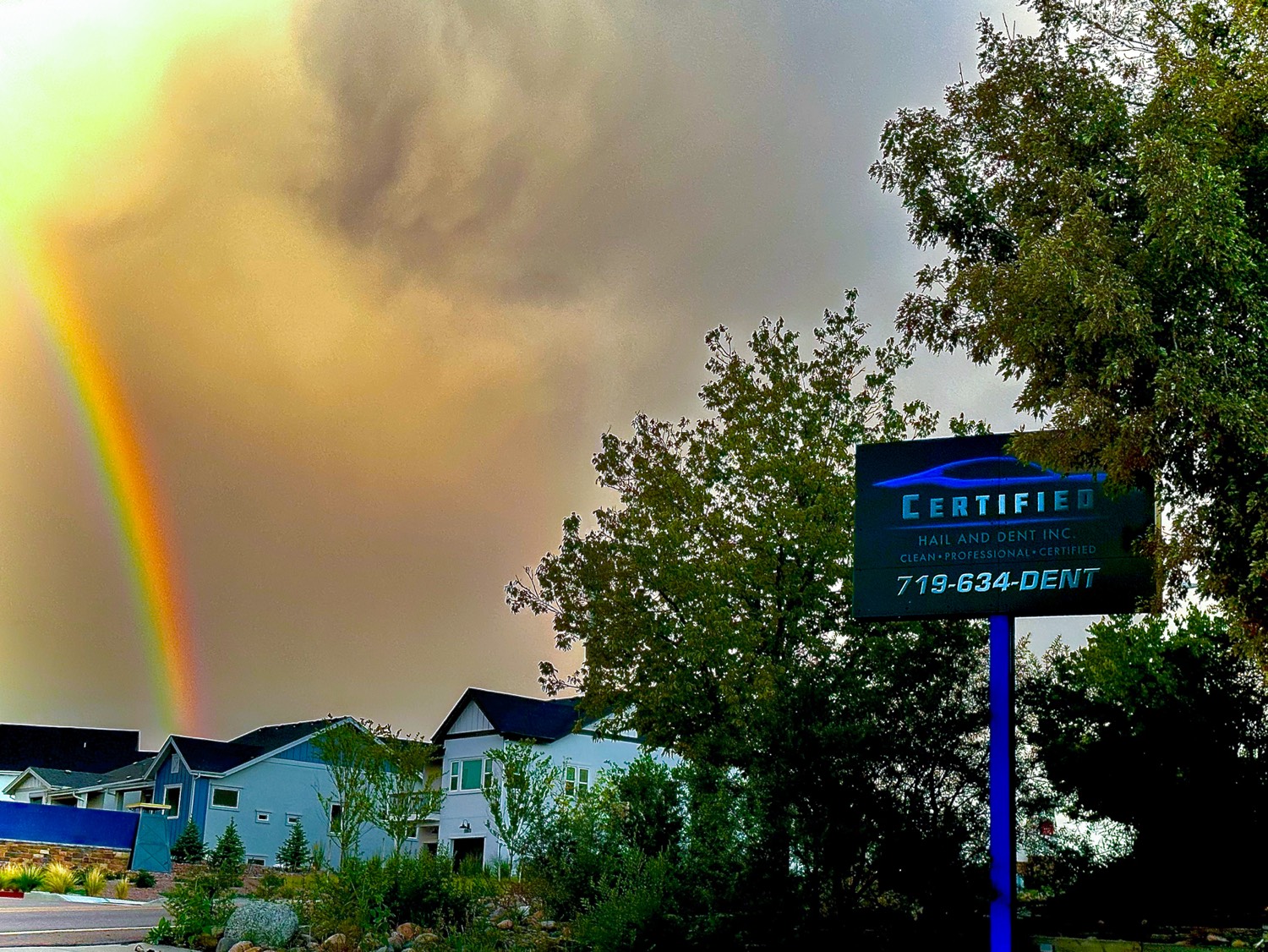 Certified Hail and Dent shop sign in Colorado Springs after a storm with a rainbow